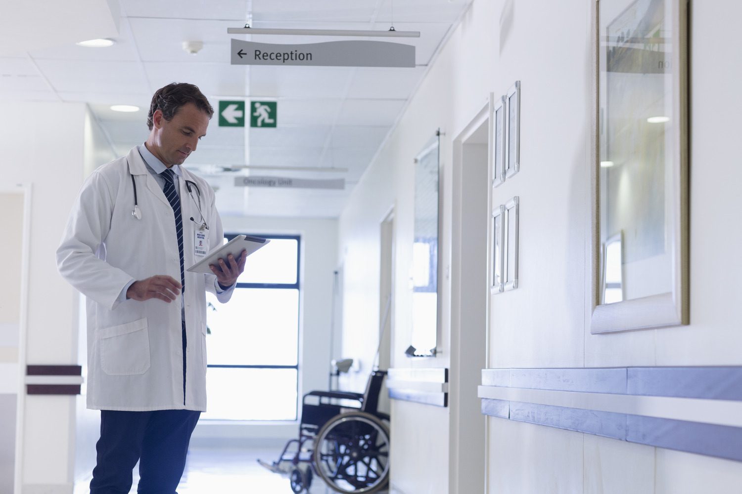 Doctor with digital tablet making rounds in hospital corridor