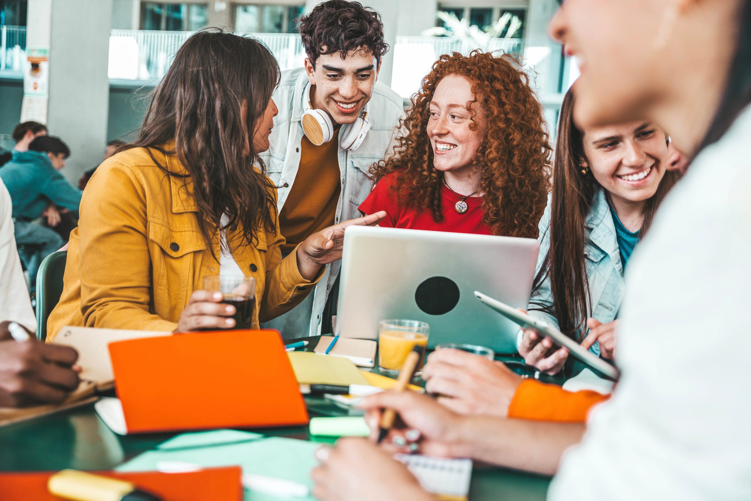Multiracial university students sitting together at table with books and laptop - Happy young people doing group study in high school library - Life style concept with guys and girls in college campus